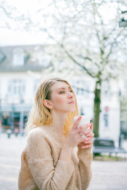 La bella giovane donna beve il caffè per andare sulla strada di una città europea