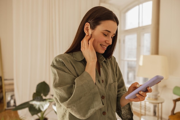 La bella giovane donna caucasica si rallegra per l'acquisto online tanto atteso utilizzando il telefono cellulare Bruna con un sorriso sul viso guarda nello smartphone Concetto di comunicazione ed emozioni positive