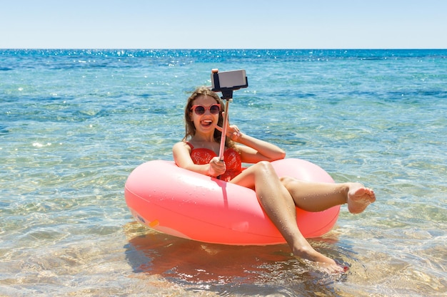 La bella giovane donna che si rilassa e fa il selfie sulla ciambella gonfiabile in mare