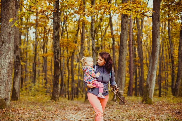 La bella giovane donna con la neonata nella foresta di autunno raccoglie il brashwood