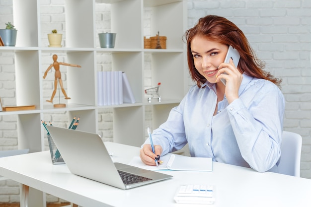 La bella giovane donna di affari sta utilizzando uno smartphone, lavorante nell&#39;ufficio