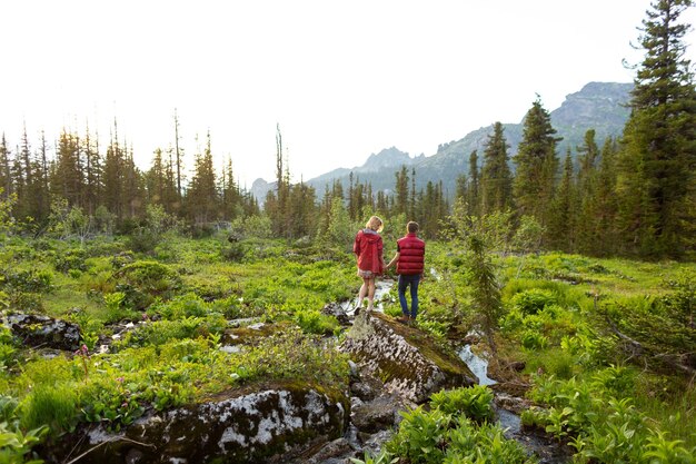 La bella giovane donna e l'uomo camminano abbracciati e baciati nella natura di montagna al tramonto