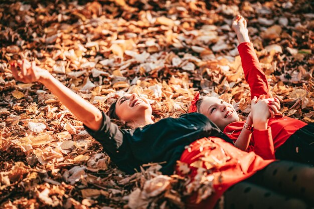 La bella giovane donna e la sua piccola figlia stanno godendo nei colori soleggiati della foresta di autunno. Sono sdraiati su foglie giallo oro e si divertono.