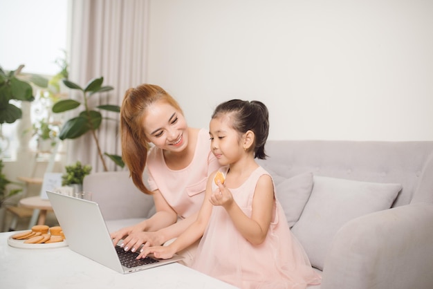La bella giovane donna e la sua piccola figlia sveglia stanno usando il computer portatile a casa