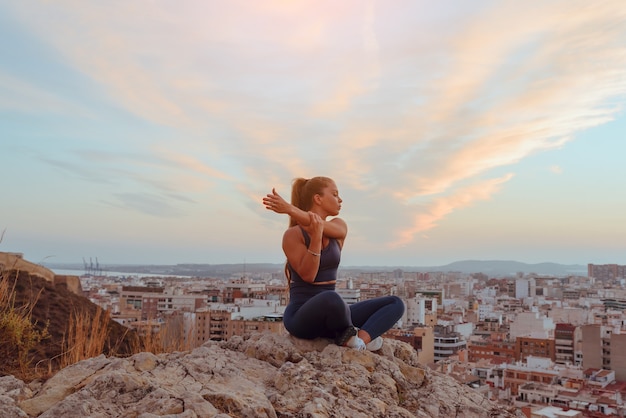 La bella giovane donna fa yoga all'aperto, in cima a un crinale di montagna in città.