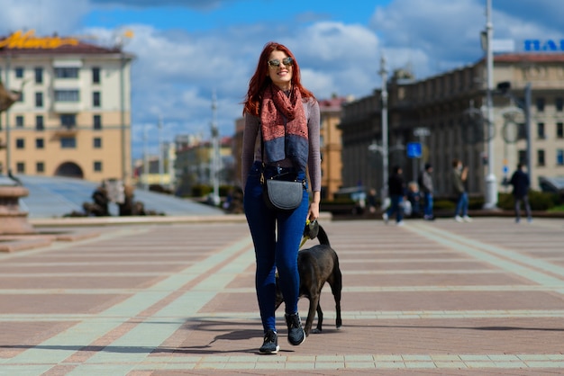 La bella giovane donna felice con il cane nero sveglio si diverte sulla strada. Concetto di amicizia tra animali e persone.