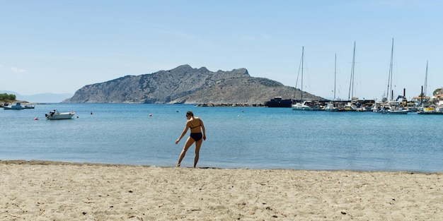 La bella giovane donna in costume da bagno si gode le vacanze estive sulla spiaggia con gli yacht sullo sfondo da vicino