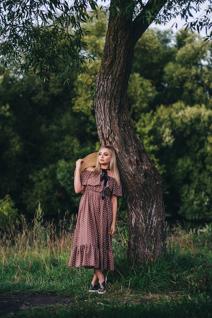 La bella giovane donna in un cappello e un vestito cammina in natura in autunno.