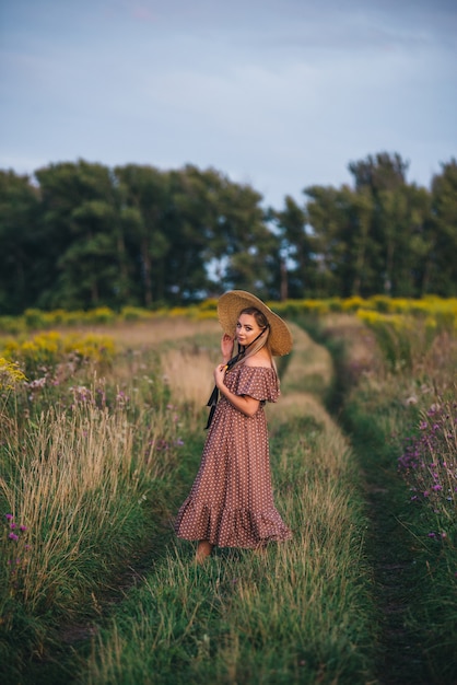 La bella giovane donna in un cappello e un vestito cammina in natura in autunno.