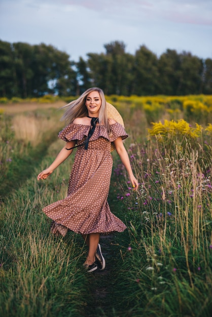 La bella giovane donna in un cappello e un vestito cammina in natura in autunno.