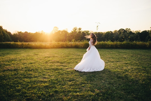 La bella giovane donna in un vestito da sposa bianco e stivali neri al tramonto è fotografata.
