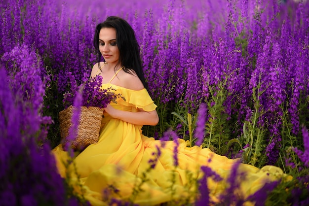 La bella giovane donna in un vestito giallo si siede in un campo di fiori viola.