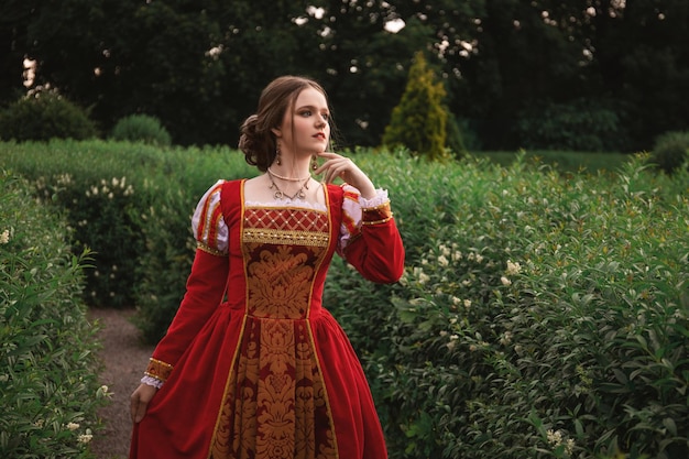 la bella giovane donna in un vestito medievale rosso sta stando nel giardino