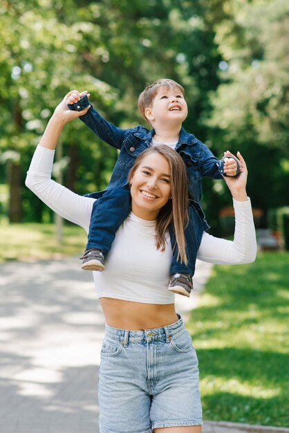 La bella giovane donna in vestiti del denim gioca con il suo piccolo figlio nel parco di estate