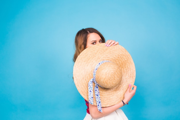 La bella giovane donna indossa in abito estivo e cappello di paglia sta ridendo su sfondo blu con spazio di copia.