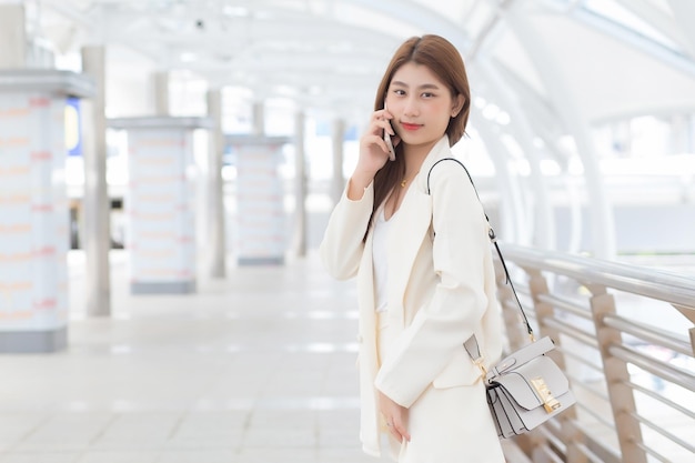 La bella giovane donna lavoratrice professionista asiatica in abito bianco sorride e tiene in mano uno smartphone