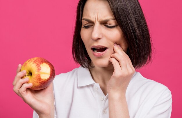 La bella giovane donna morde una grande mela e ha mal di denti