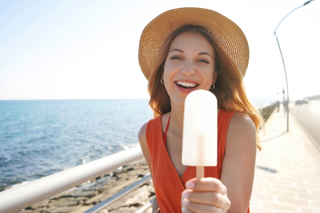 La bella giovane donna offre un ghiacciolo al limone alla macchina fotografica in estate