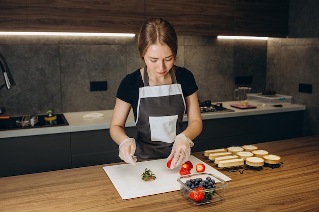 La bella giovane donna pasticcera prepara dolci su uno sfondo di cucina moderna