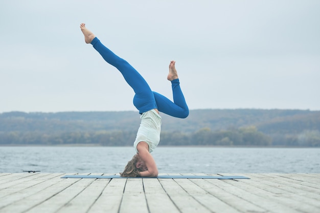 La bella giovane donna pratica l'asana Shirshasana di yoga