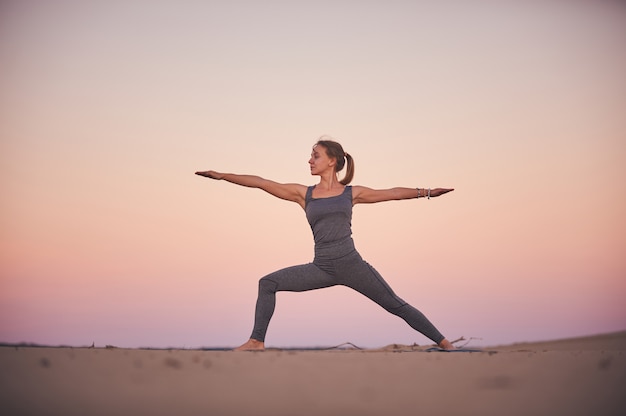 La bella giovane donna pratica l'asana Virabhadrasana di yoga