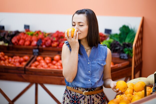 La bella giovane donna sceglie le arance in un deposito di verdure