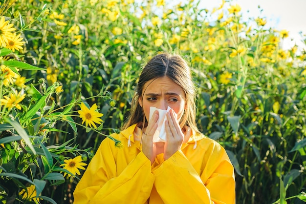 La bella giovane donna sexy si trova sulla priorità bassa dei fiori. Ragazza che starnutisce e tiene un fazzoletto di carta in una mano e un bouquet di fiori nell'altra. Influenza.