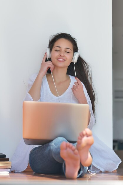 la bella giovane donna si rilassa e lavora al computer portatile mentre ascolta musica sulle cuffie e legge il libro a casa