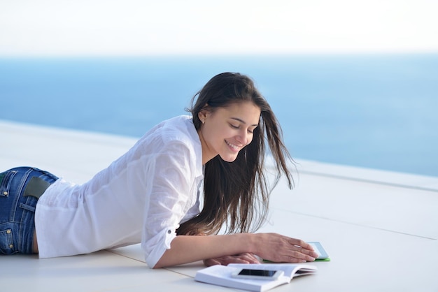 la bella giovane donna si rilassa e lavora al computer portatile mentre ascolta musica sulle cuffie e legge il libro a casa