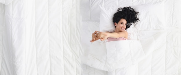 La bella giovane donna sorridente si trova sul grande letto con la biancheria pastello bianca