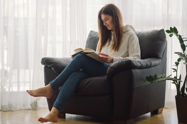 La bella giovane donna sta leggendo un libro a casa
