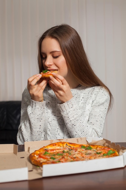 La bella giovane donna sta mangiando la pizza nell'ufficio