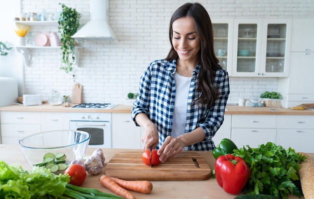 La bella giovane donna sta preparando l'insalata di verdure in cucina. Cibo salutare. Insalata Vegana. Dieta. Concetto di dieta. Uno stile di vita sano. Cucinare A Casa. Prepara da mangiare. Tagliare gli ingredienti sul tavolo