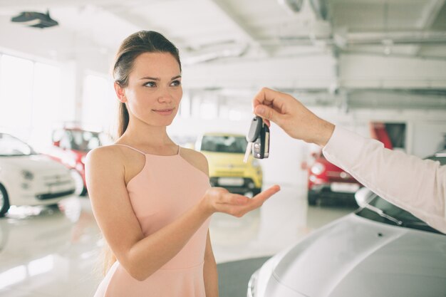 La bella giovane donna sta tenendo una chiave nel concessionario auto.