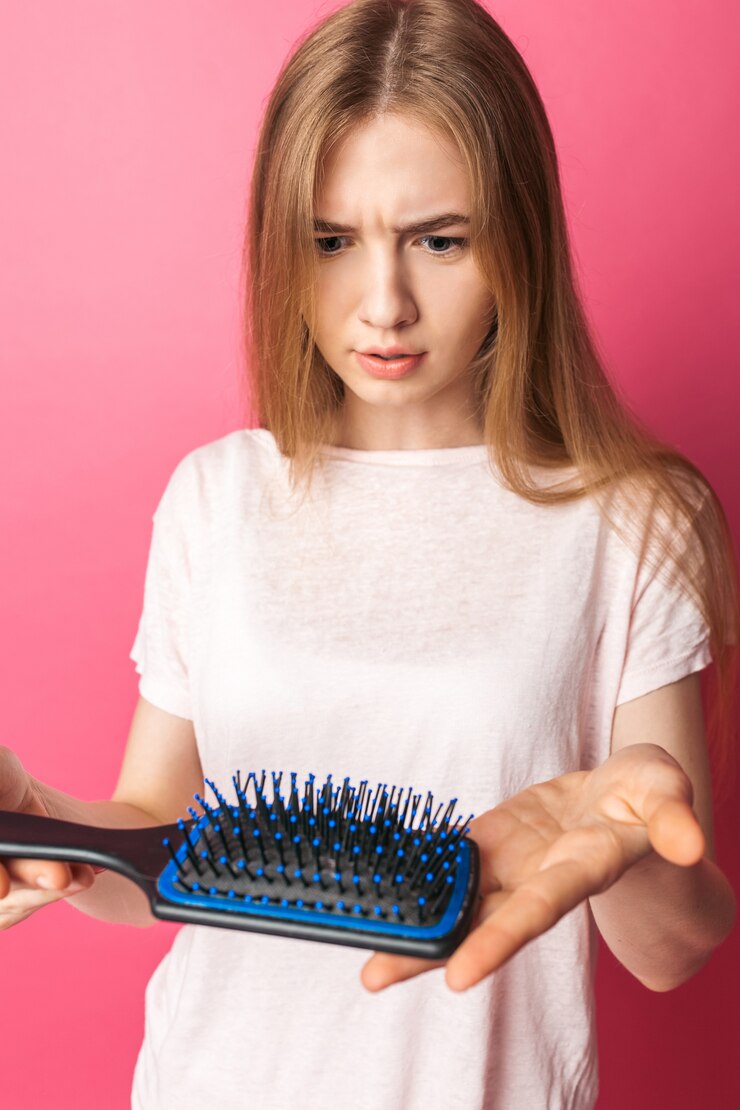 La bella giovane donna triste che mostra il pettine, capelli cade, sulla parete isolata rosa, fine su
