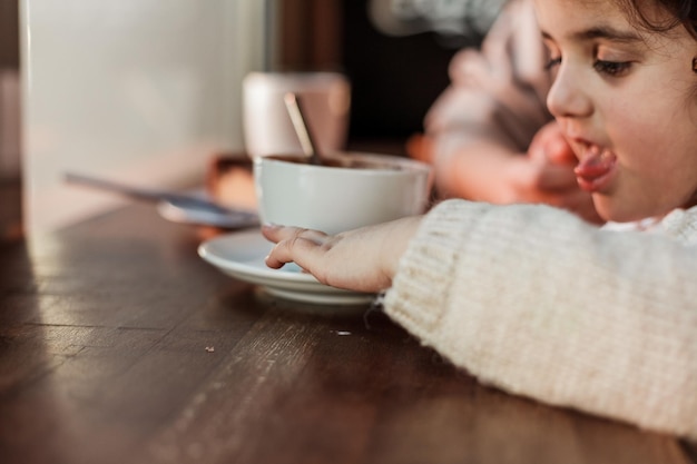 La bella giovane madre dai capelli rossi con la figlia carina dai capelli ricci è seduta in un caffè accogliente e beve la calda festa della mamma al caldo della scuola