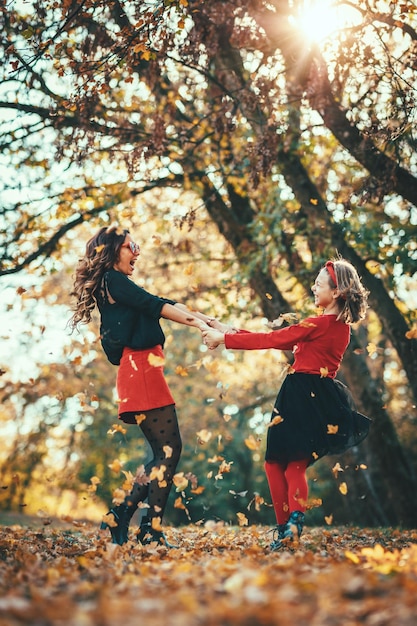 La bella giovane madre e sua figlia felice si divertono nella foresta al tramonto. Si tengono per mano, ridono e si girano.