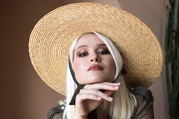 La bella giovane modella bionda sta posando in cappello di paglia e camicetta trasparente verde