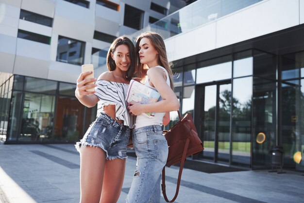 La bella giovane ragazza felice dello studente due con lo zaino vicino alla città universitaria dell'università e fa la foto del selfie. Concetto di educazione e tempo libero
