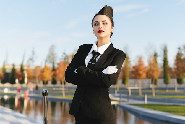 La bella hostess della giovane donna in uniforme alza gli occhi al cielo e aspetta il suo volo nel parco