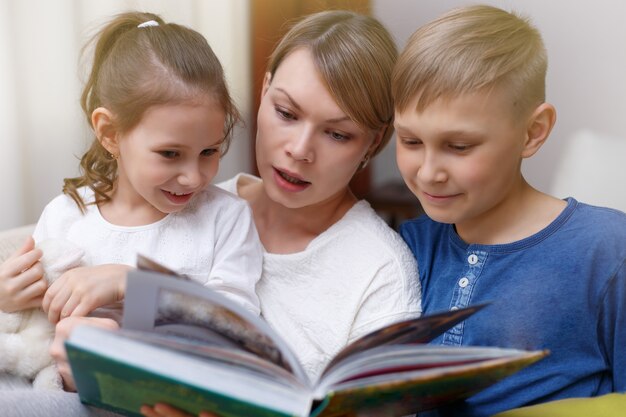 La bella madre sta leggendo un libro ai suoi bambini piccoli. Sorella e fratello stanno ascoltando una storia. Felice famiglia amorevole.