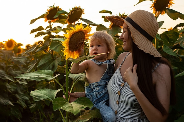 La bella madre tiene in braccio un bambino in un campo di girasoli. tenerezza, sorrisi, felicità.