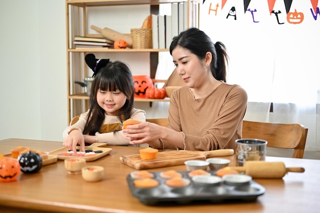 La bella mamma asiatica e sua figlia stanno preparando i cupcakes di Halloween Concetto di giorno di Halloween