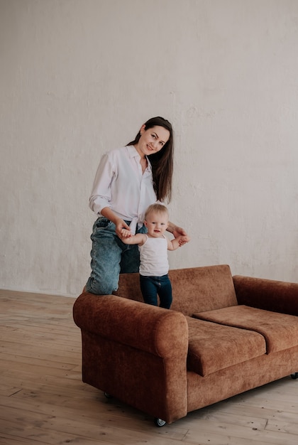 La bella mamma bruna gioca con la sua piccola figlia su un divano marrone