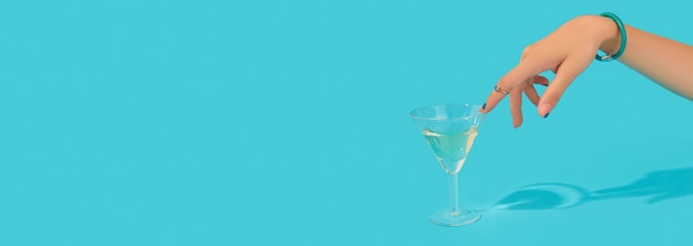 La bella mano della donna curata con l'anello alla moda tocca il bicchiere di cocktail su sfondo blu