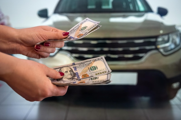 La bella mano di un uomo sano tiene una somma rotonda di banconote da un dollaro vicino a nuove auto costose in uno showroom di automobili. Concetto di affari. Il concetto di scelta