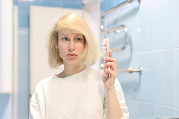 La bella modella femminile soddisfatta si pettina i capelli con la spazzola per capelli, ha una carnagione ben curata e una pelle sana. Cura dei capelli e concetto di routine di bellezza