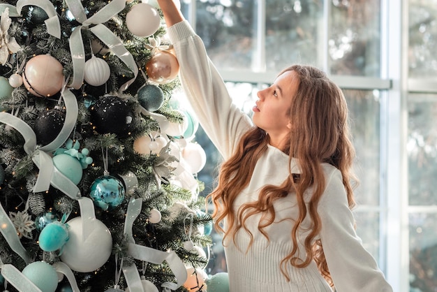 La bella ragazza adolescente sta decorando l'albero di Natale in casa. Buon Natale e buone feste concetto.