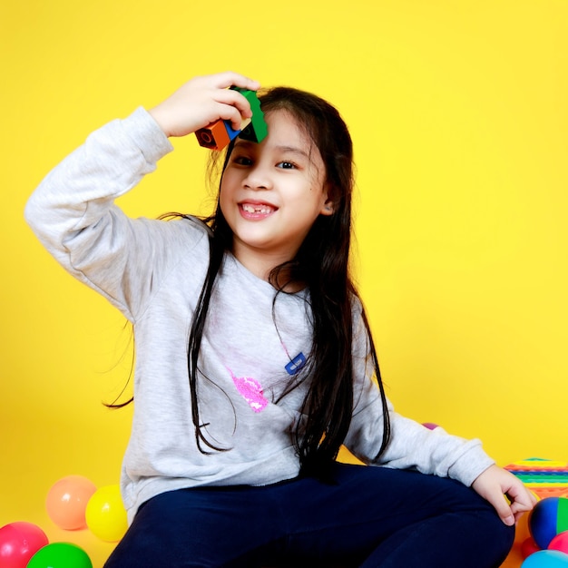 La bella ragazza asiatica sul maglione si diverte a giocare con i bambini per assemblare e collegare blocchi di plastica come gioco divertente per mostrare l'immaginazione creativa mentre si è seduti nel cortile della scuola di palline colorate e giocattoli