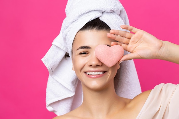 La bella ragazza attraente allegra con un asciugamano sulla sua testa tiene una spugna sotto forma di cuore rosa